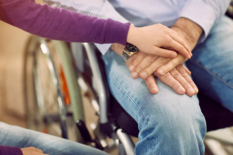 woman touching the hands of a loved one in a wheelchair.webp